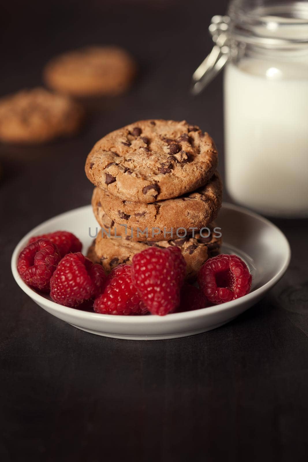 Chocolate chip cookies with red raspberry and milk on rustic wood background. Homemade dessert.
