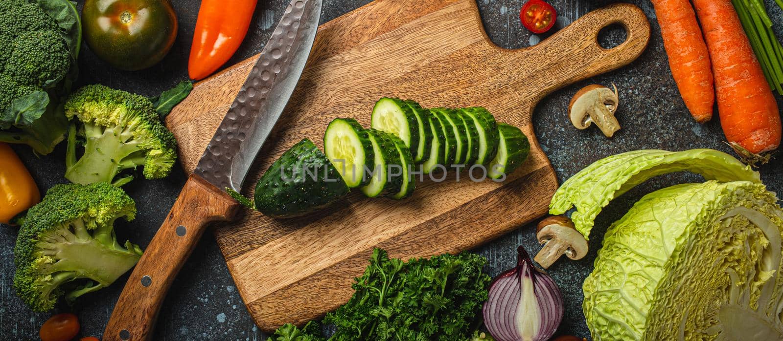 Chopped cucumber on wooden cutting board with knife and assorted fresh vegetables by its_al_dente