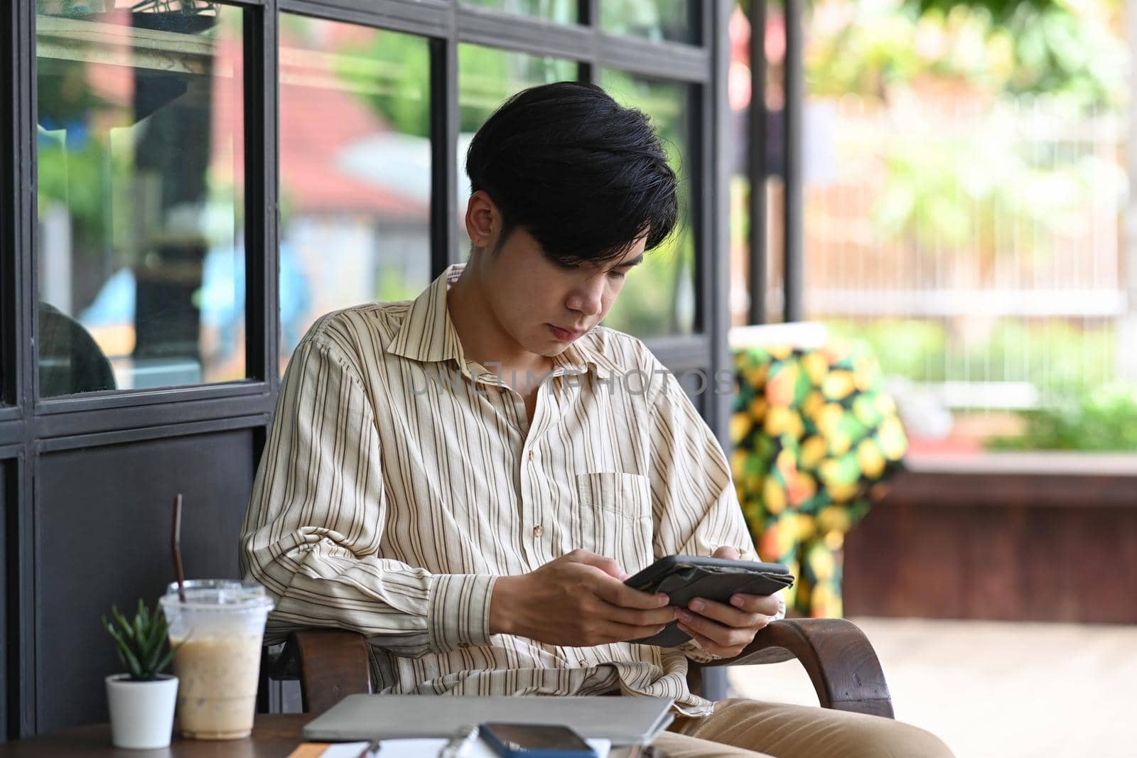 Young Asian man sitting outdoor cafe and using digital tablet. by prathanchorruangsak