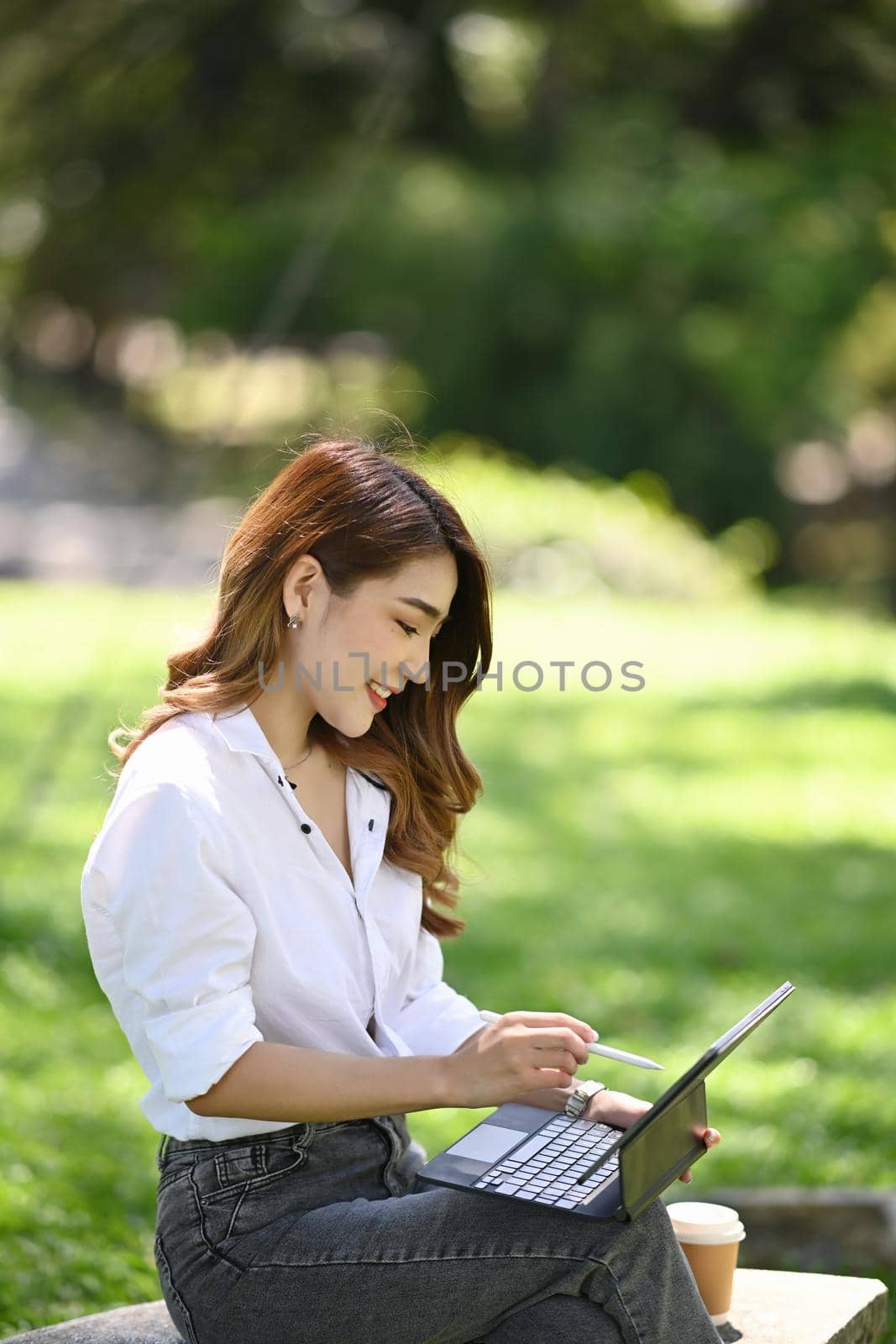 Beautiful woman sitting on bench in the city park and working with computer tablet.