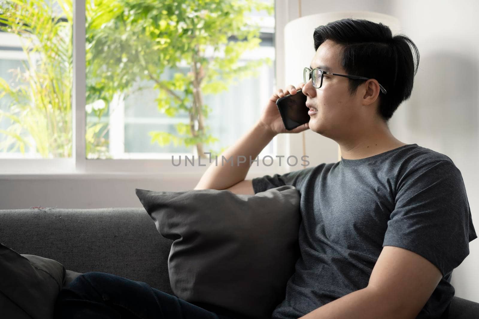 Handsome man sitting in living room and talking on mobile phone. by prathanchorruangsak