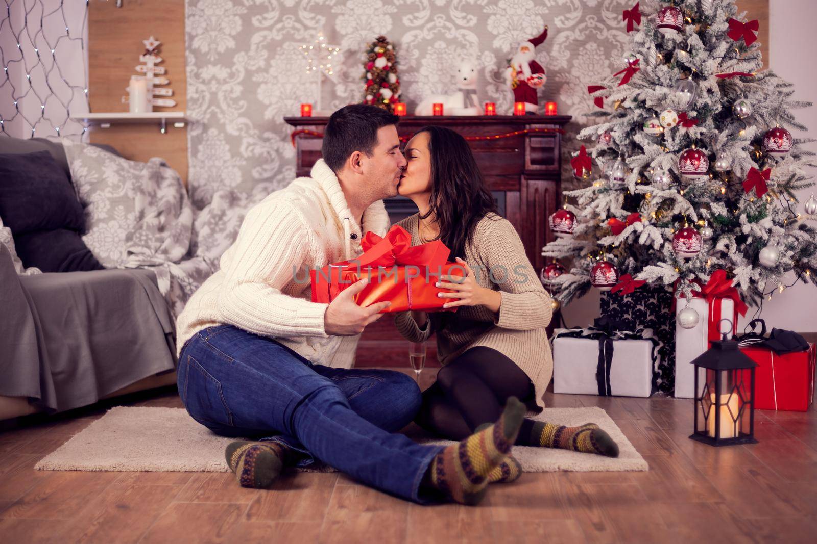 Beautiful young couple kissing near a christmas tree in a cozy home by DCStudio