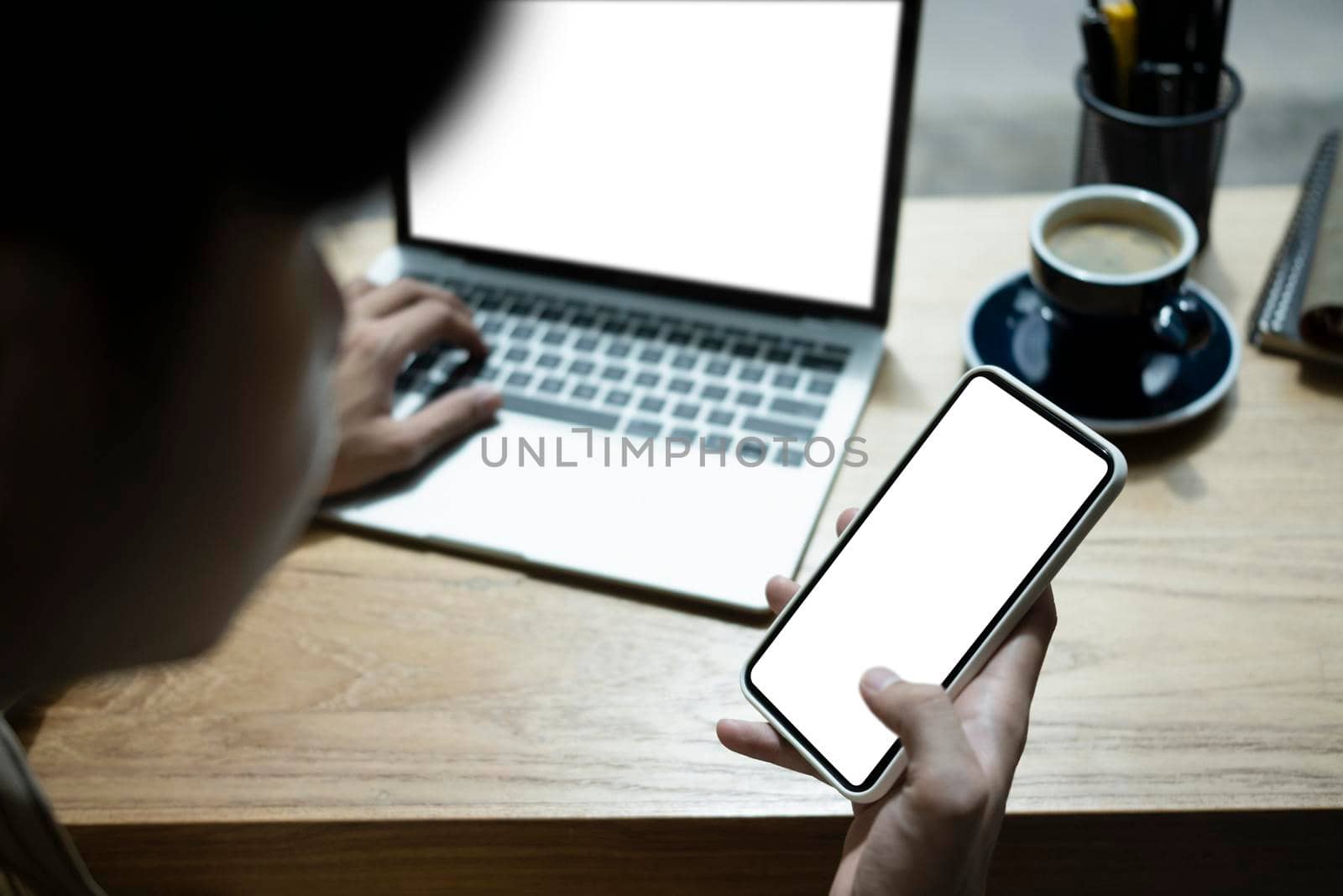 Close up view young man holding mobile phone and working with laptop computer.