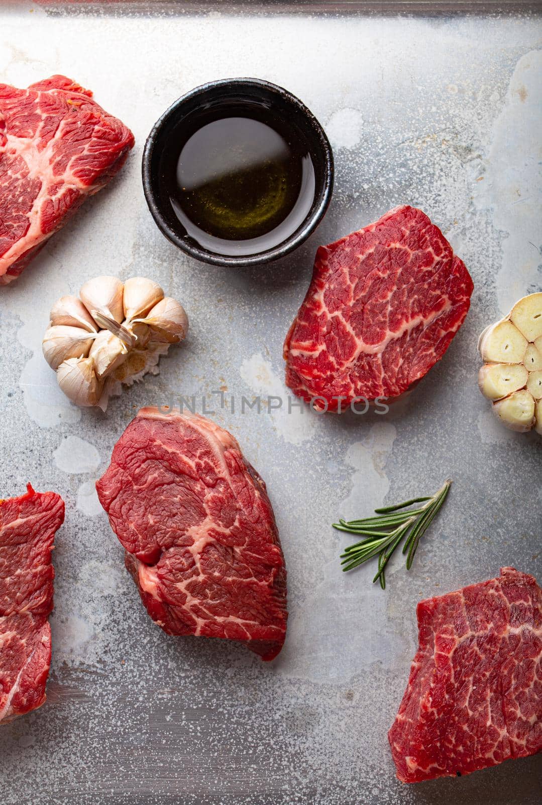 Raw uncooked meat beef cubes for stew or roasting with seasonings, olive oil, garlic and fresh rosemary on rustic aluminum baking tray from above