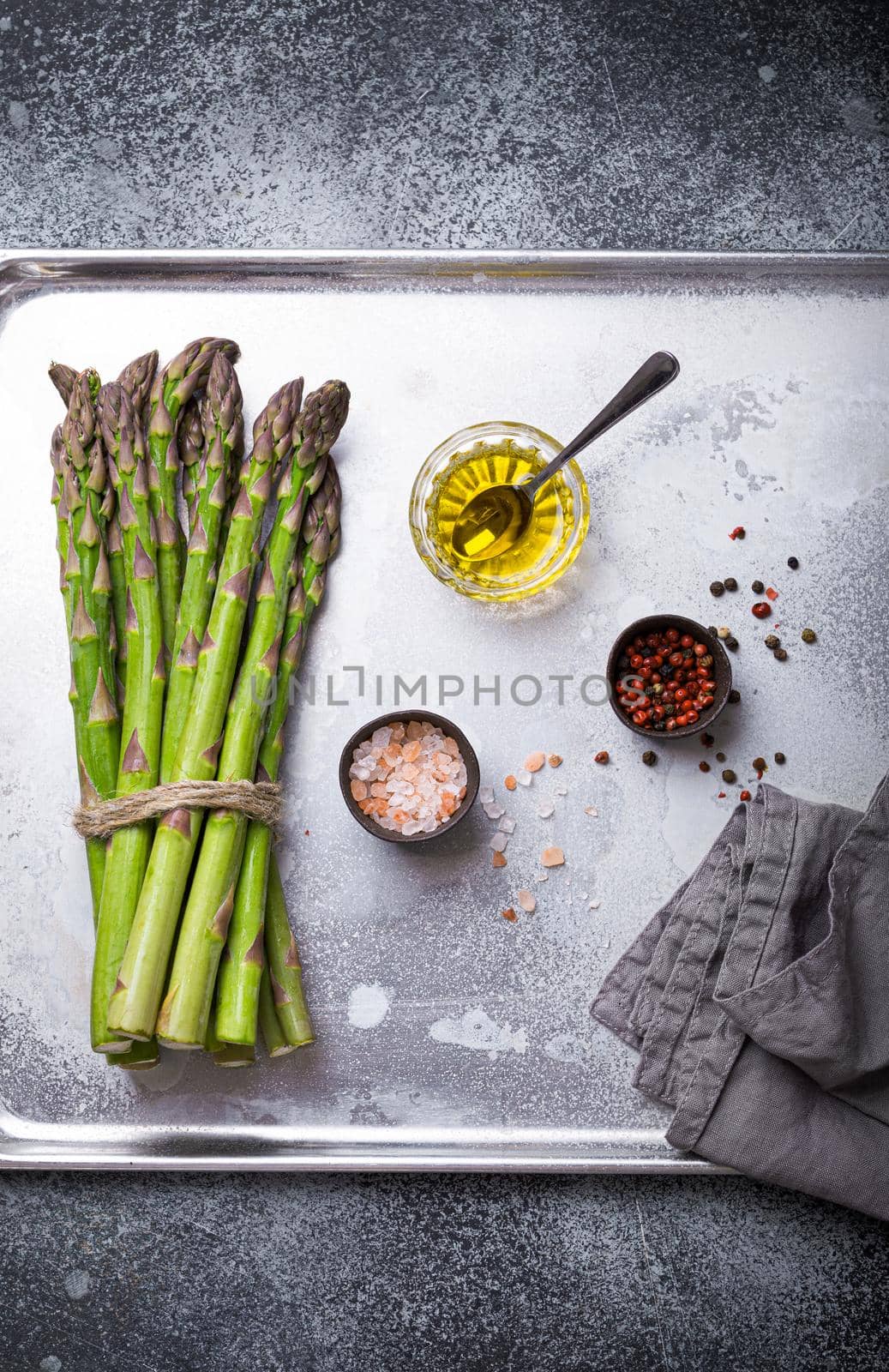 Bunch of fresh green organic asparagus ready for cooking on baking tray with olive oil and seasonings, top view, close up. Asparagus for clean and healthy diet and eating  .