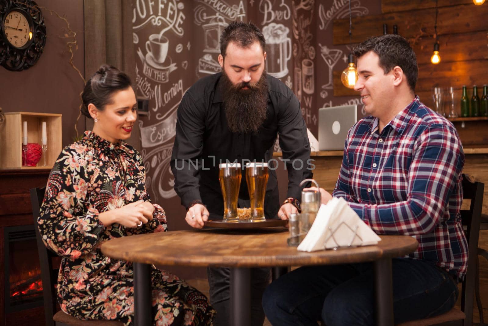 Hipster barman giving the order to beautiful young couple.Great Pub.