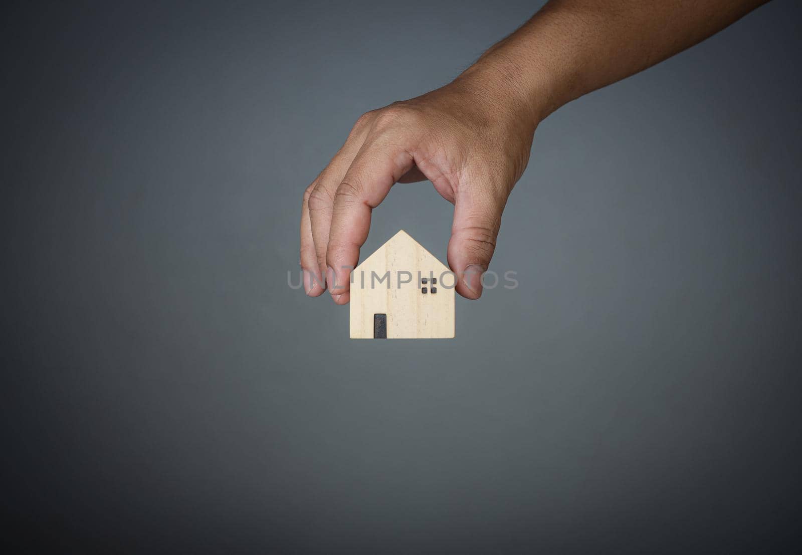 Concept of selling a house. A hand is holding a model house on a gray background. Real estate agent offer house, property insurance and security, affordable housing concepts, home insurance broker agent, salesman person. by Unimages2527