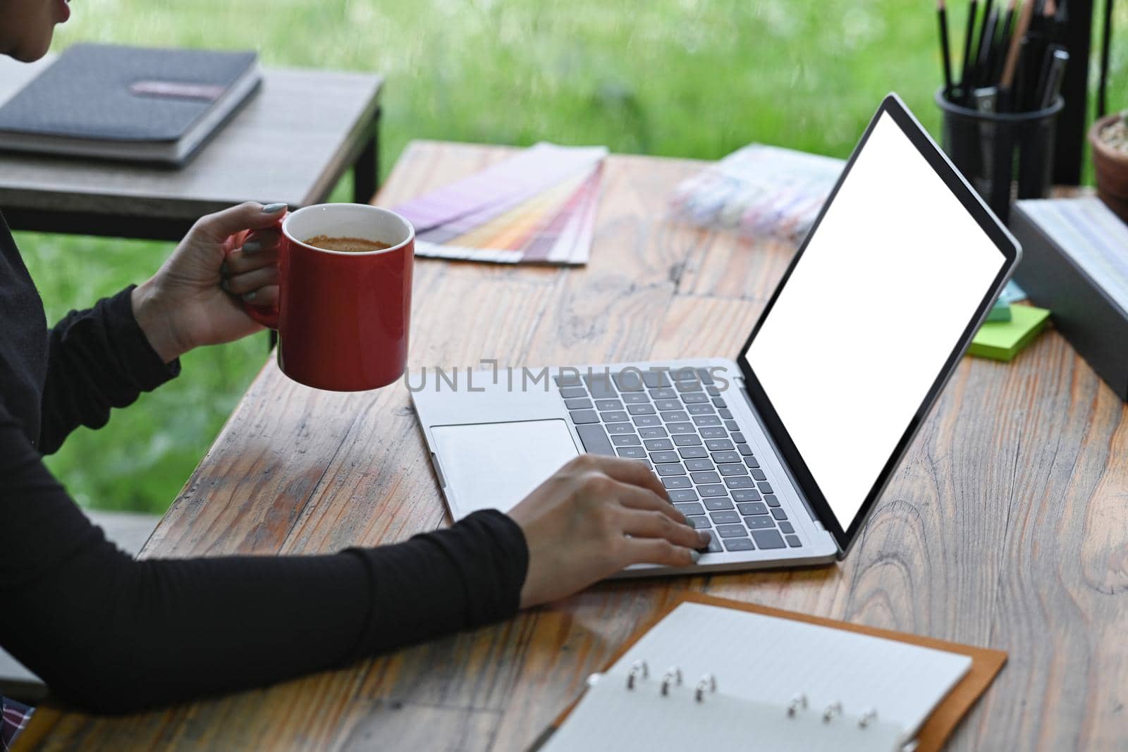 Female designer holding coffee cup and working with laptop computer.