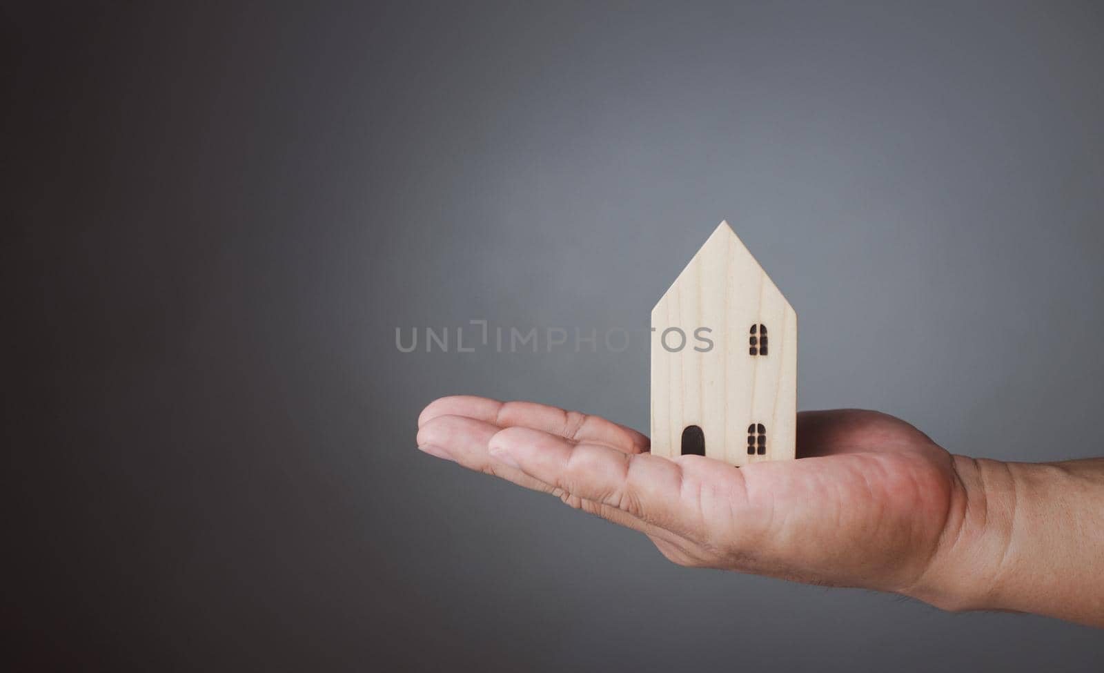Concept of selling a house. A hand is holding a model house on a gray background. Real estate agent offer house, property insurance and security, affordable housing concepts, home insurance broker agent, salesman person.