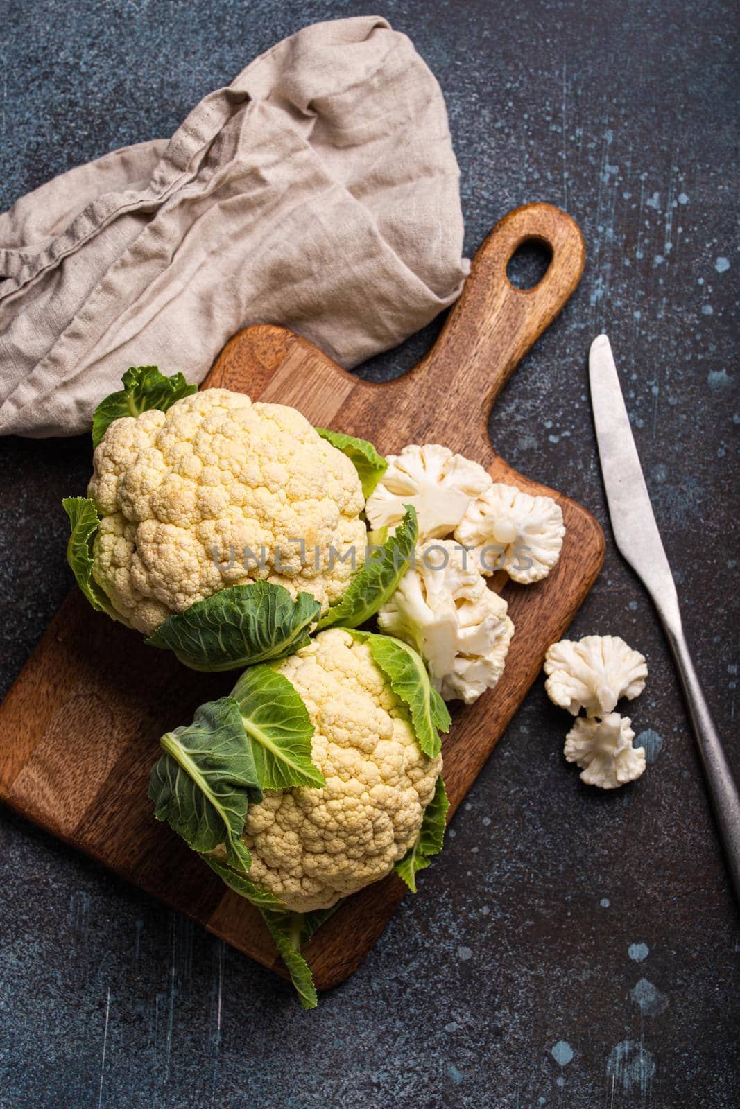 Fresh organic cut cauliflower on wooden cutting board with kitchen knife, ready to be cooked, top view with copy space. Vegetarian food, clean eating concept .