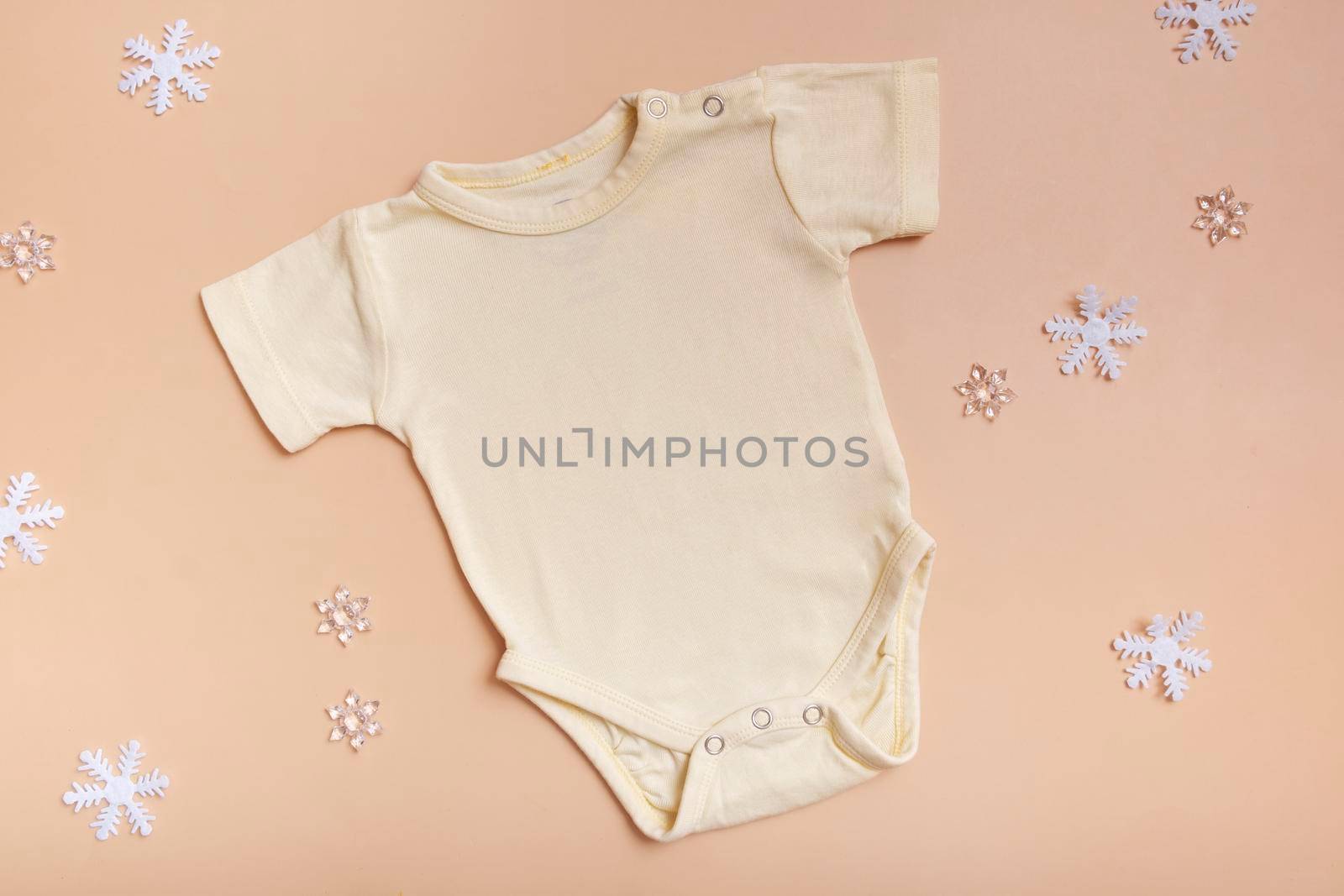 Yellow baby bodysuit mockup for logo, text or design on pink background with winter decotations top view. by ssvimaliss