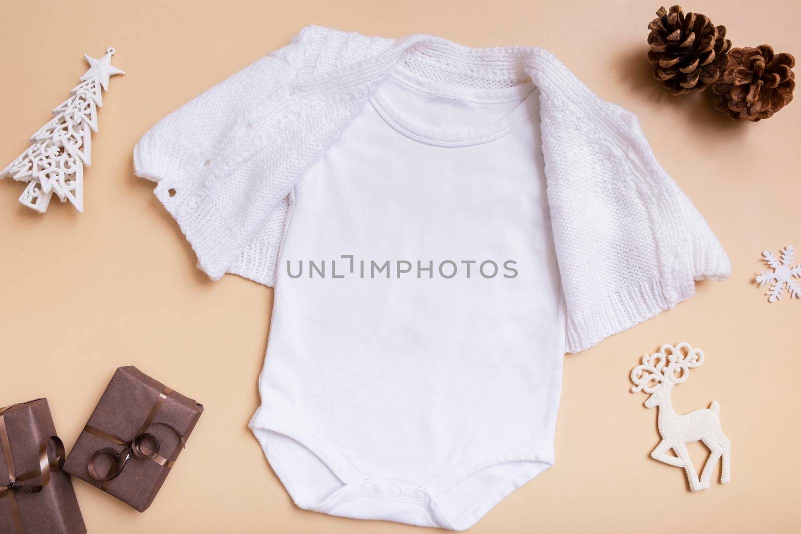 White baby bodysuit mockup for logo, text or design on beige background with winter decotations top view.