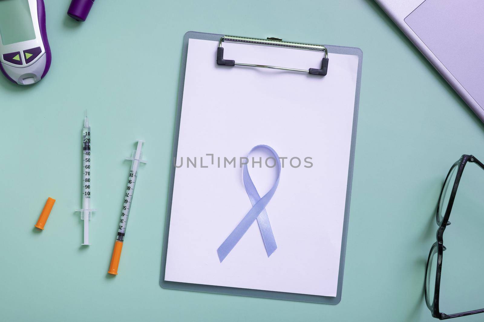 Blue ribbon and glucometer, medical supplies on color background top view with copy space. World diabetes day concept by ssvimaliss