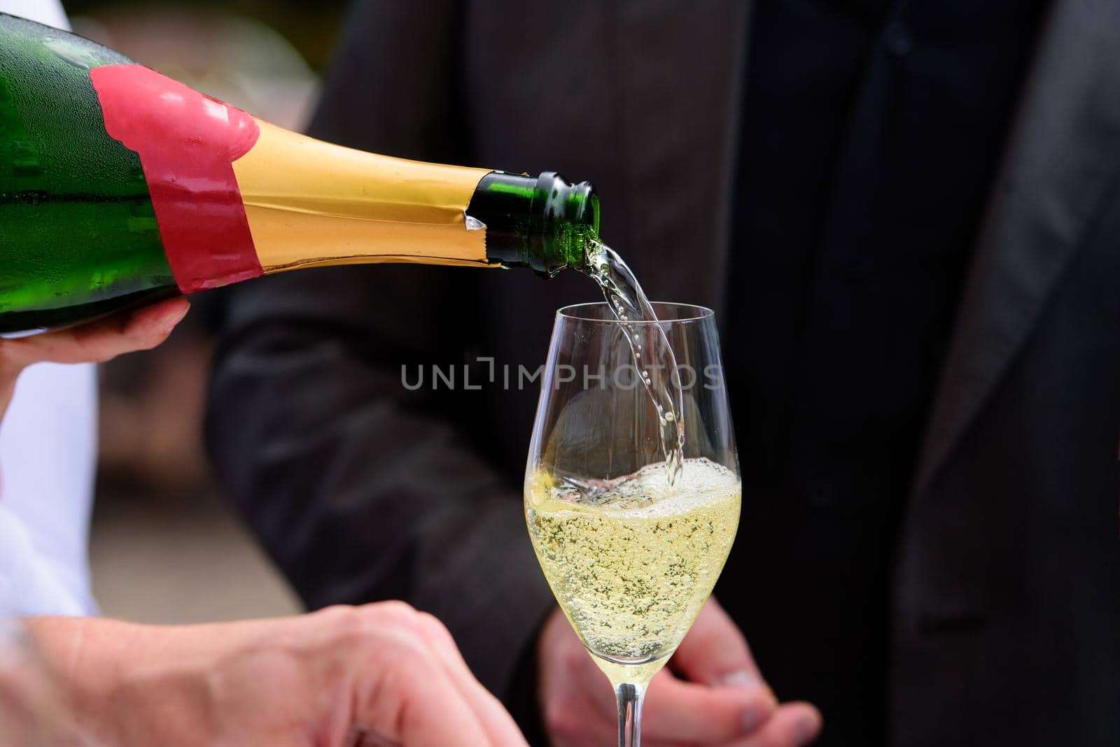 closeup of a champagne bottle pooring champagne into a champagne flute against a blurred person at a party