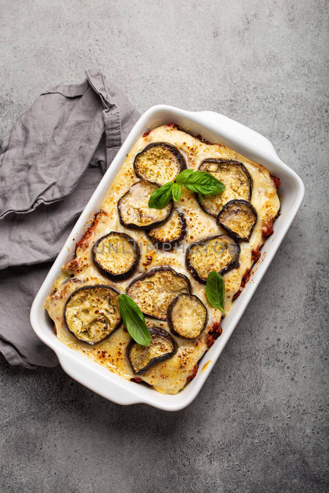 Greek mediterranean dish Moussaka with baked eggplants, ground beef in white ceramic casserole on rustic stone background from above, traditional dish of Greece