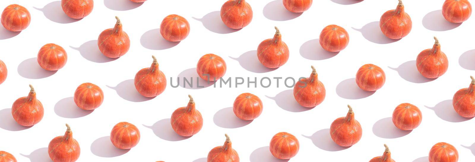 Pattern made from orange pumpkins with hard shadows on white background. Banner format.