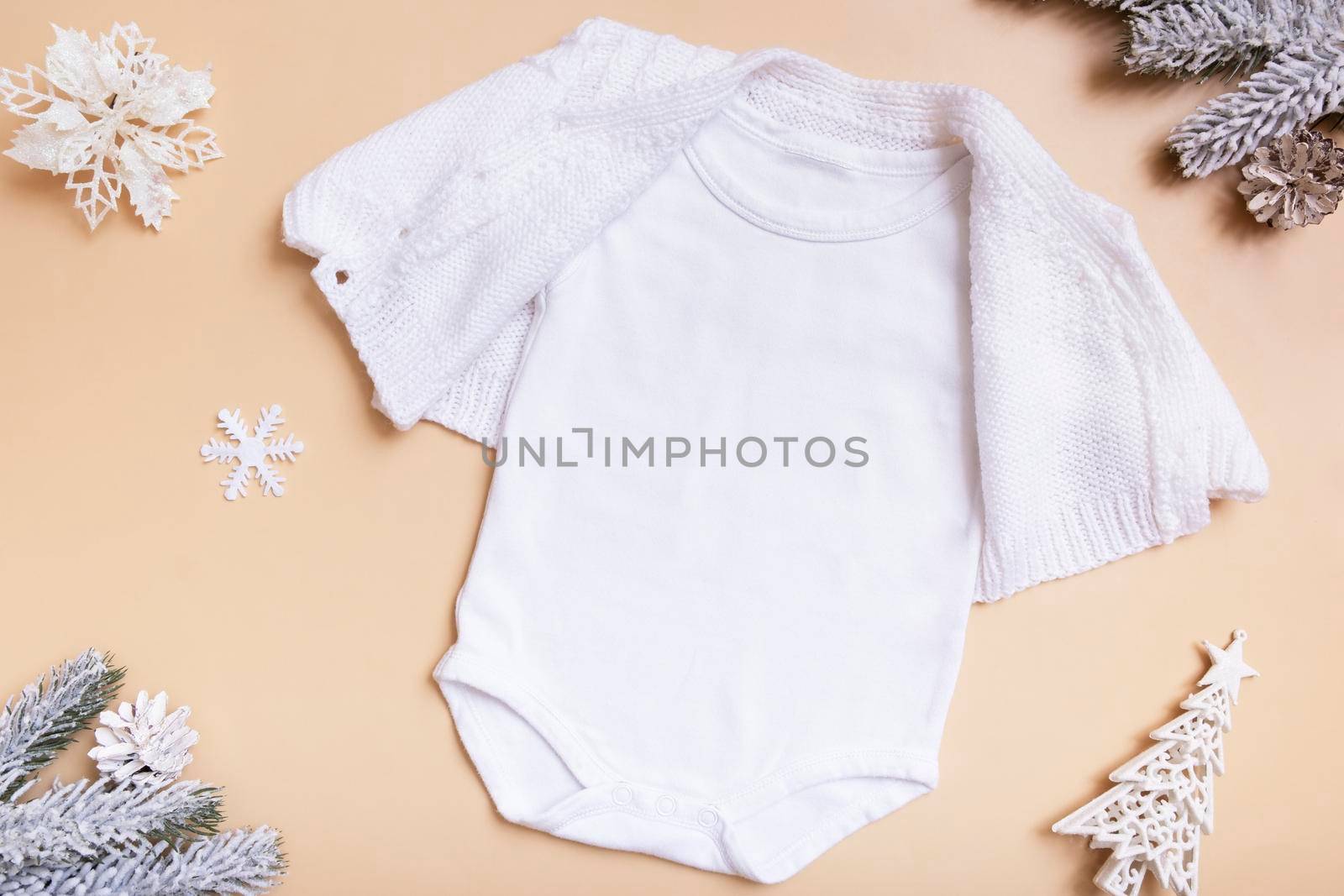 White baby bodysuit mockup for logo, text or design on beige background with winter decotations top view.