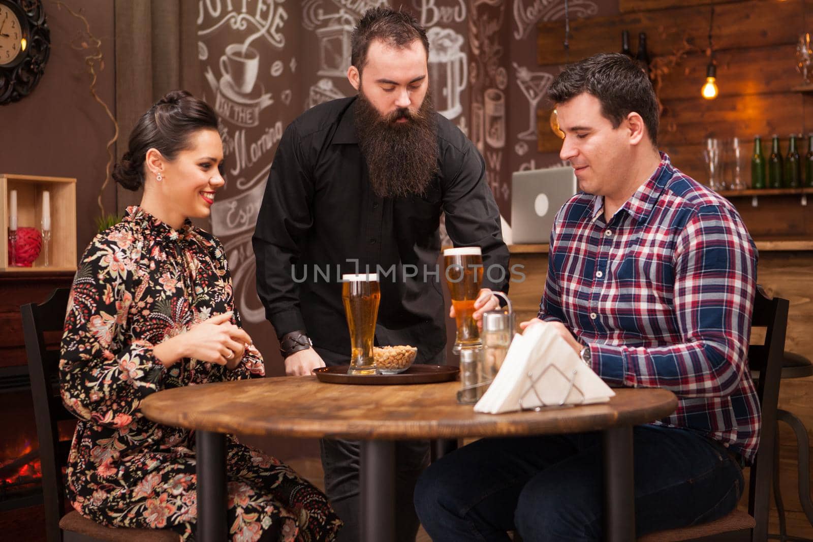 Hipster barman giving the order to beautiful young couple. by DCStudio