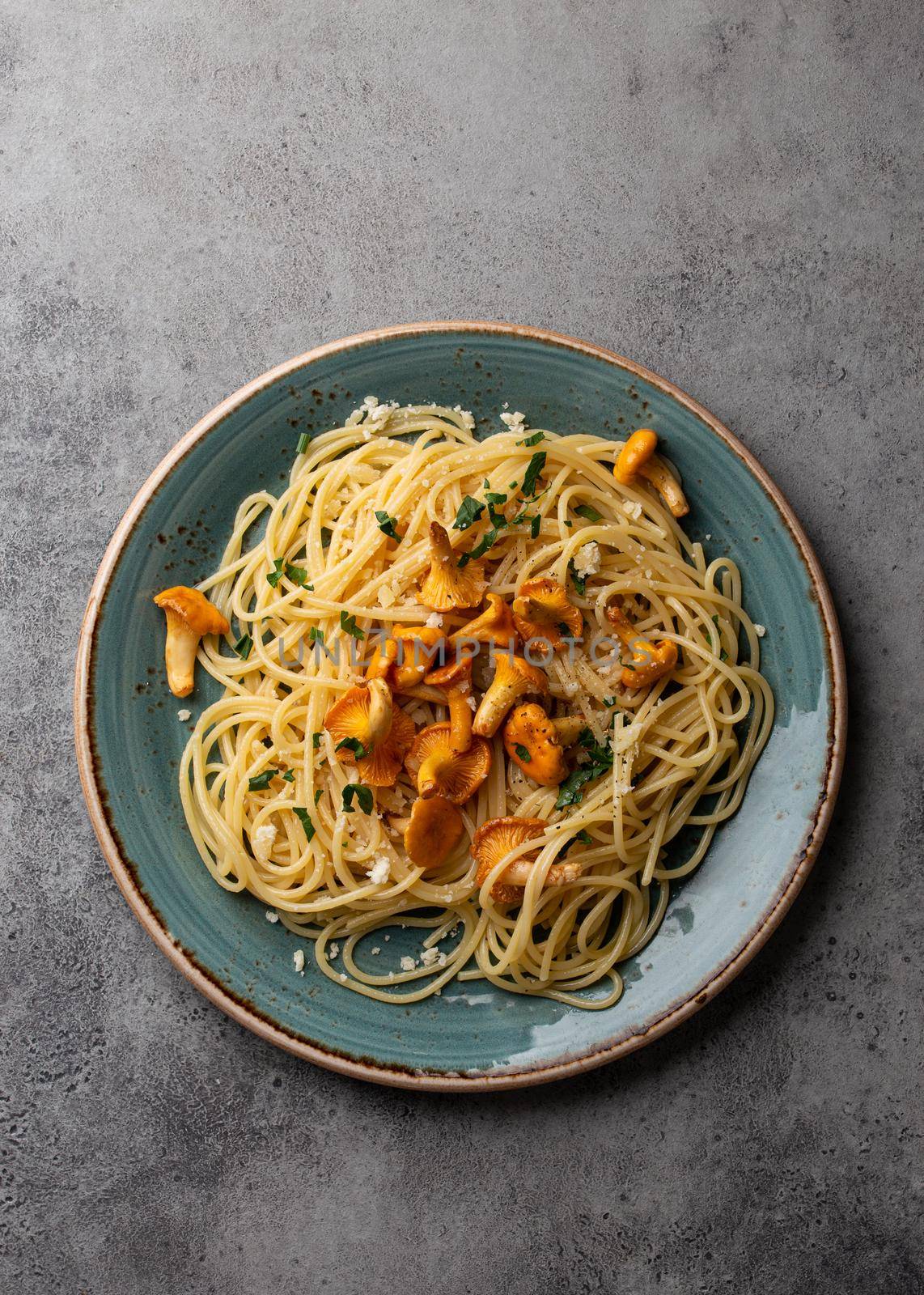 Pasta spaghetti with wild forest mushrooms chanterelles on plate. Seasonal autumn dish on rustic concrete background from above. Meal with aromatic fall chanterelles