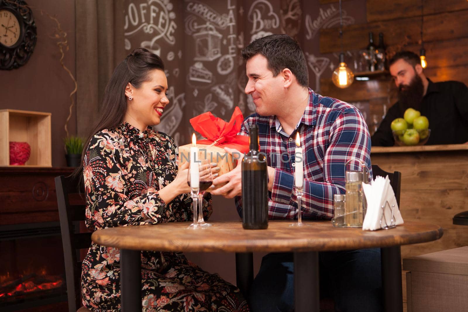 Happy husband giving wife a present in a hipster pub. by DCStudio