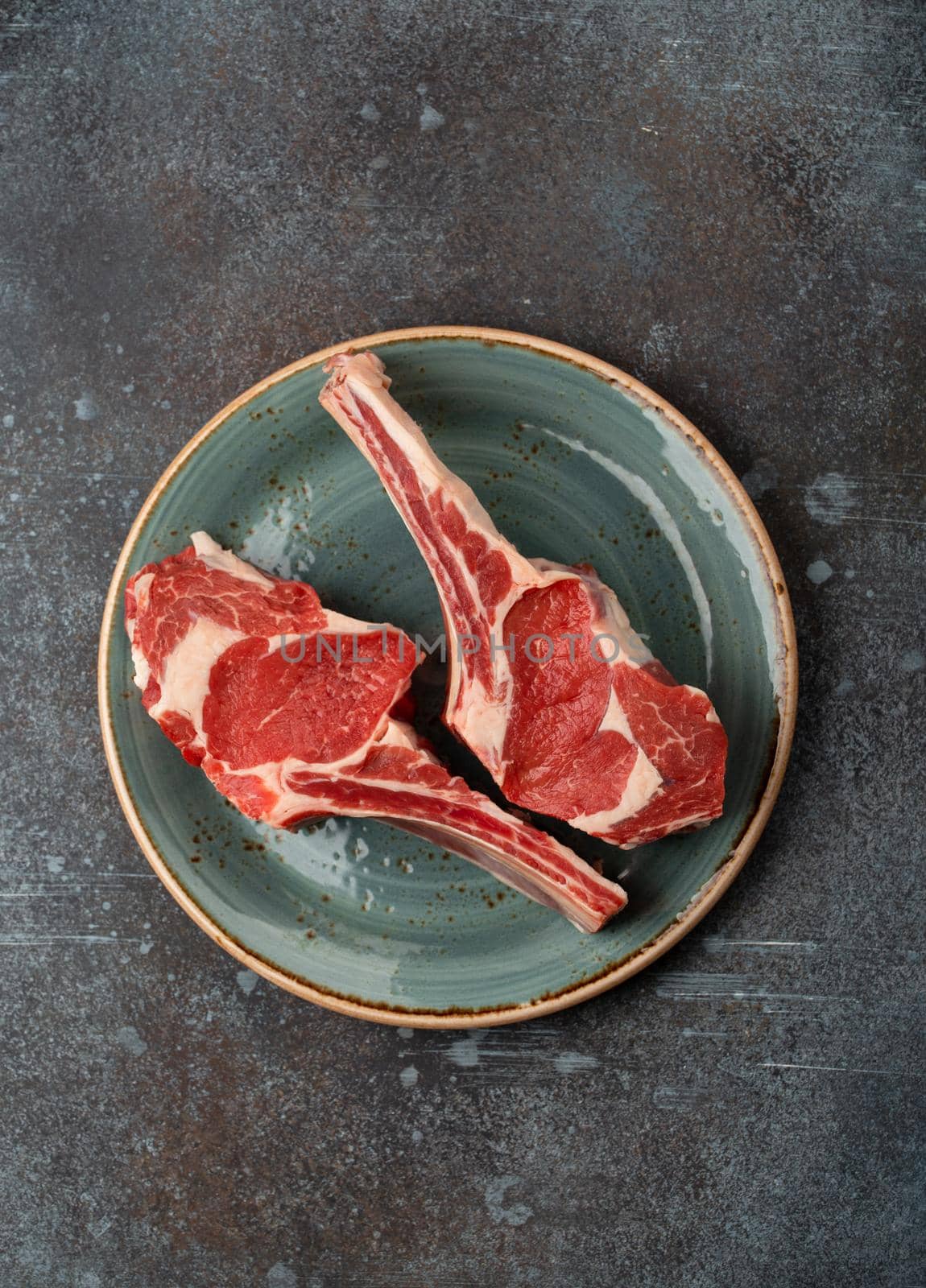 Two raw marbled Tomahawk meat steaks on plate, concrete background. Premium Beef steak on bone preparation, top view, steak house restaurant or butchery concept .