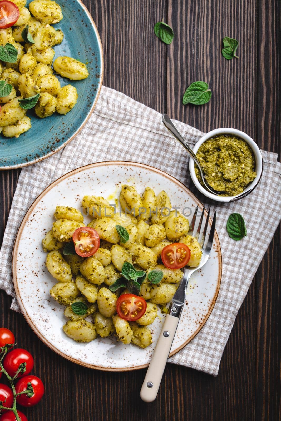 Gnocchi in plates with green pesto sauce, tomatoes and herbs on rustic wooden background, close up, top view. Traditional dish of Italian cuisine