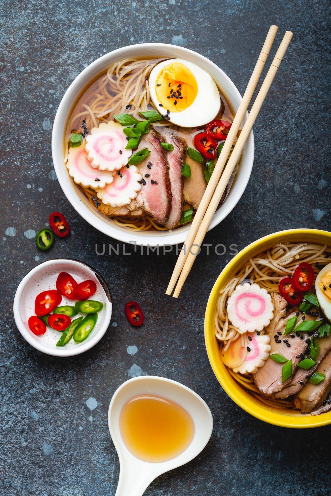 Cooking Japanese noodle soup ramen. Ramen with sliced pork, narutomaki, egg and kitchen spoon with broth on rustic stone background. Making traditional dish of Japan, top view, close-up, concept