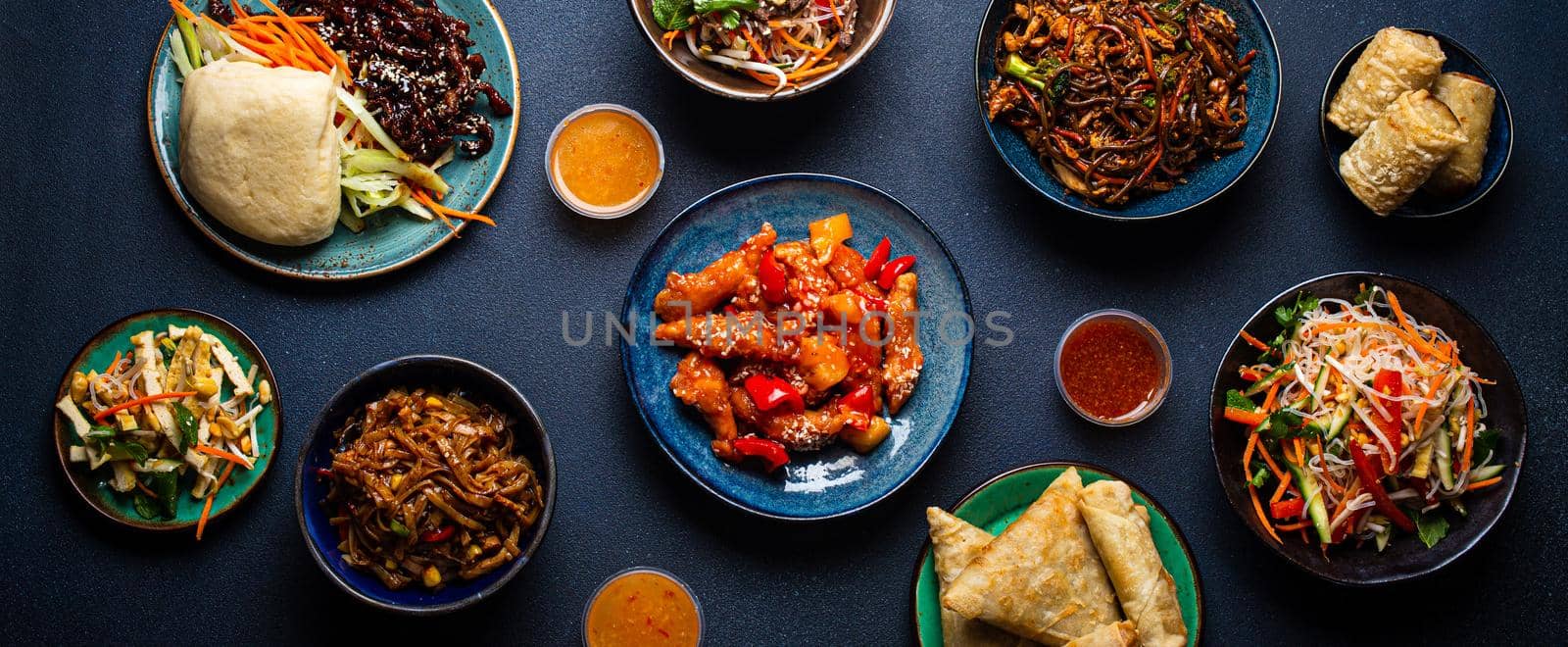 Set of assorted Chinese dishes on table: sweet and sour chicken on plate, fried spring rolls, noodles, salad, rice, steamed buns with bbq glazed pork, Asian style banquet or buffet, top view .