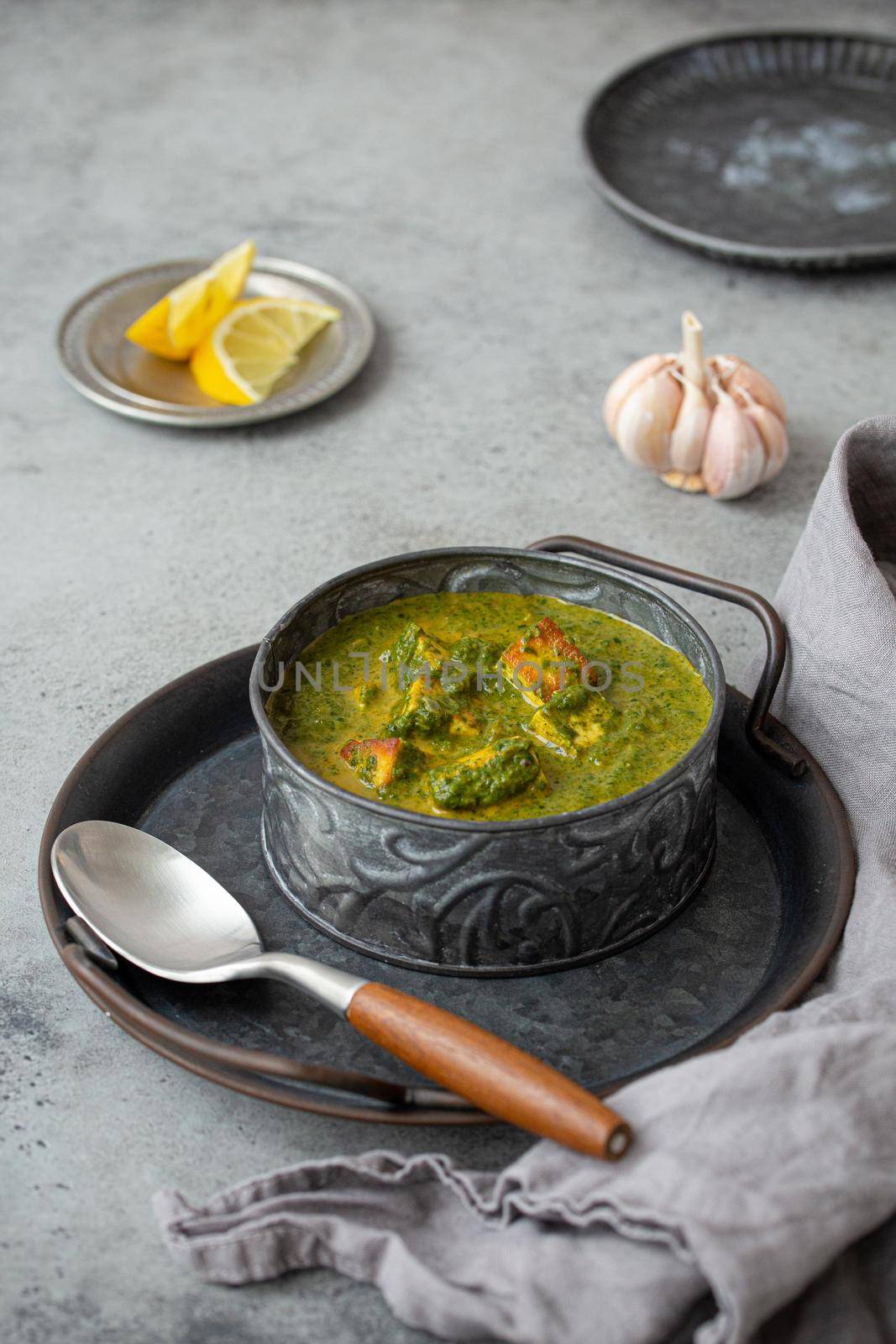 Traditional vegetarian Indian Punjabi food Palak Paneer with spinach and cheese in vintage metal bowl with spoon on rustic grey concrete background table, angle view