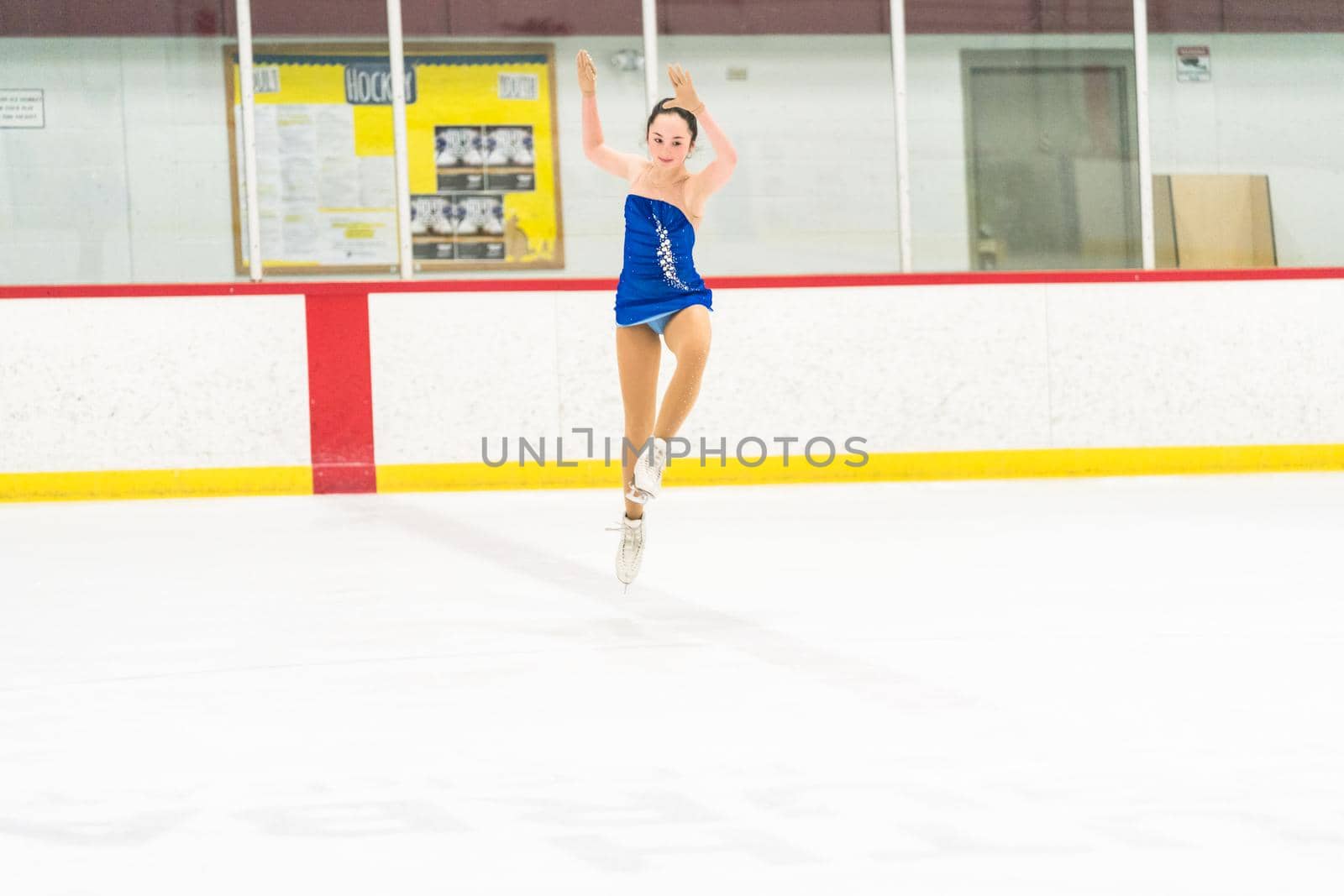 Teenage girl practicing figure skating on an indoor ice skating rink.