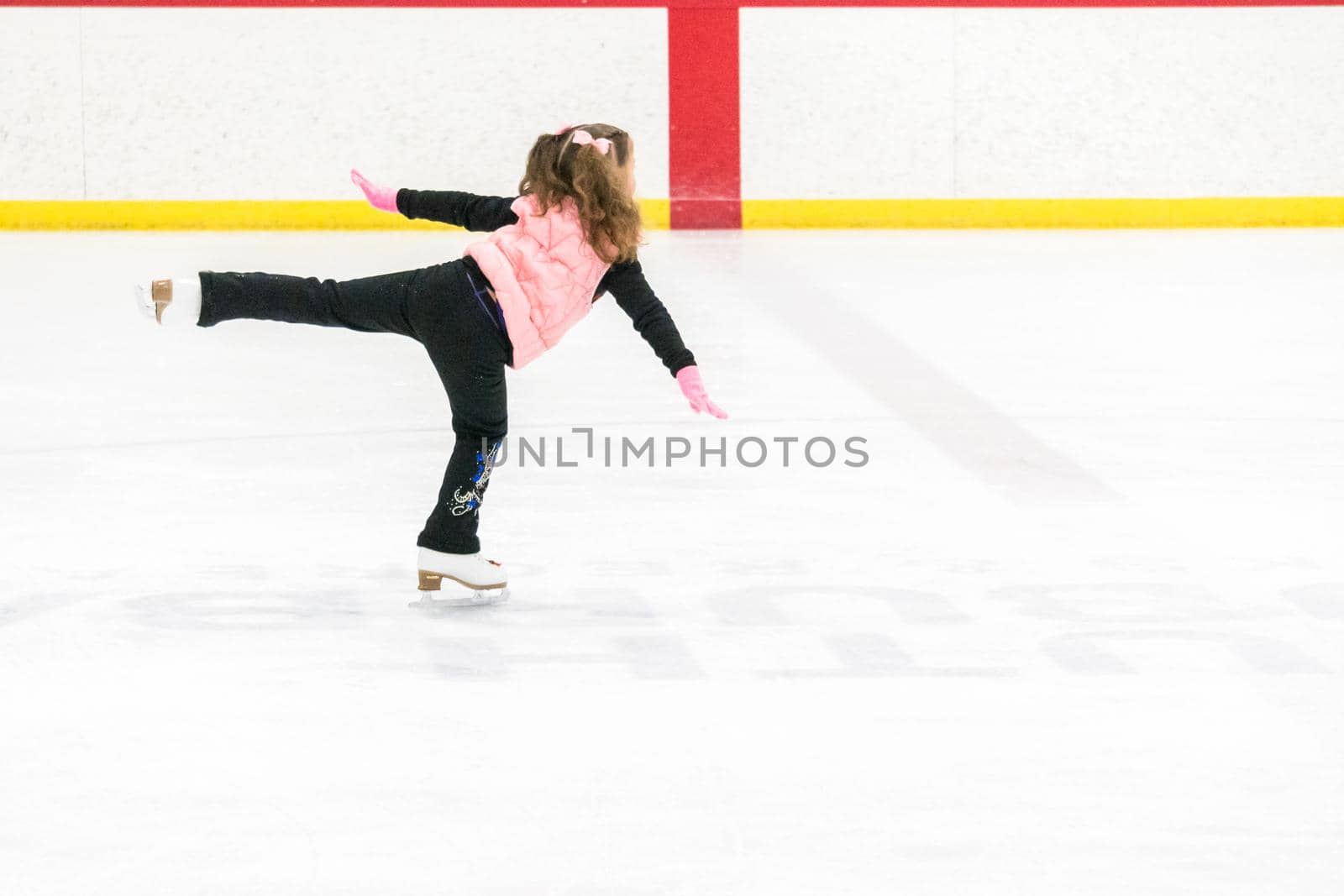 Little girl practicing figure skating moves on the indoor ice rink.