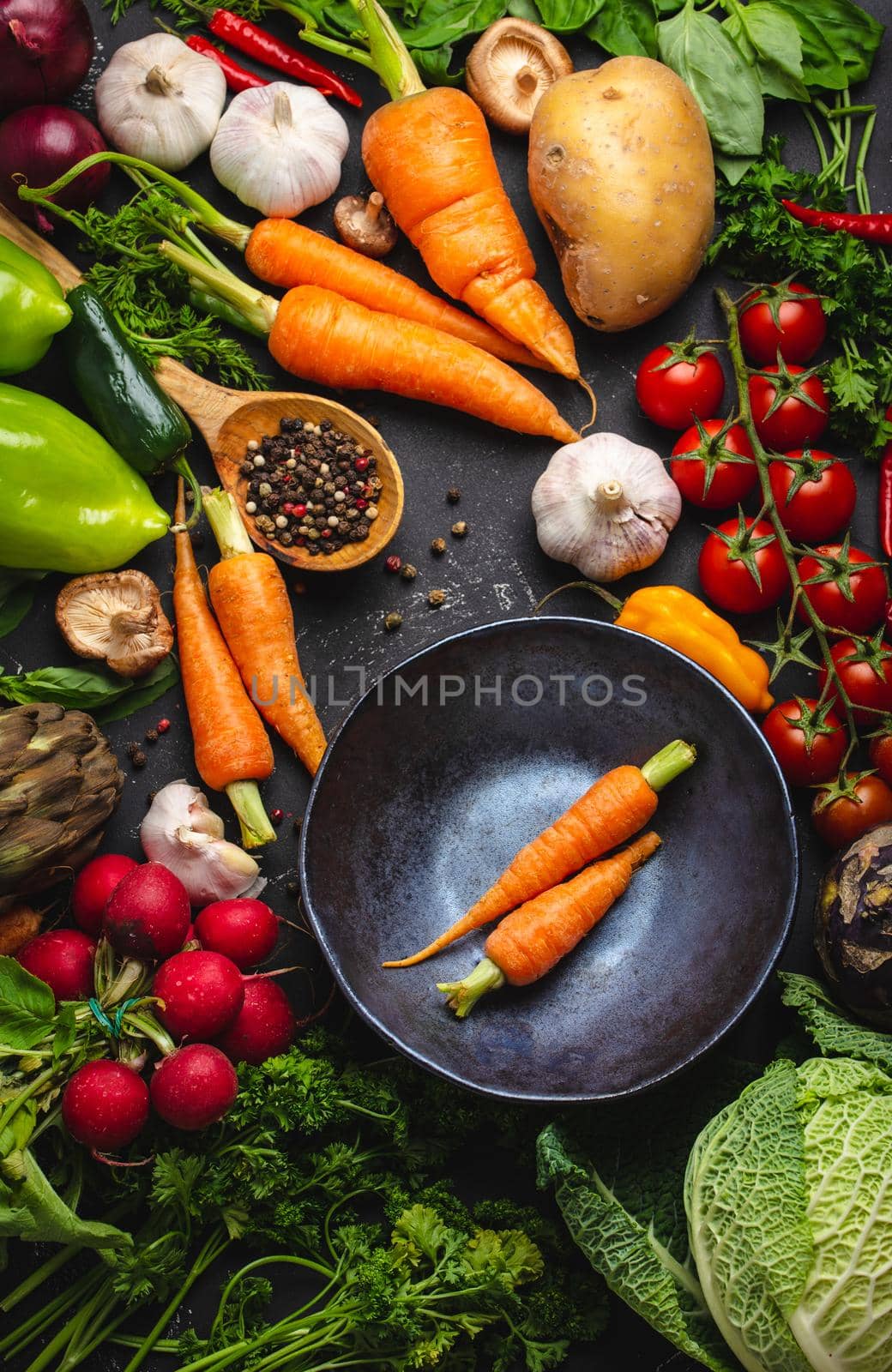 Two fresh farm carrots in vintage bowl and assorted organic vegetables on rustic black concrete background. Autumn harvest, vegetarian food or cooking clean healthy meal concept, top view