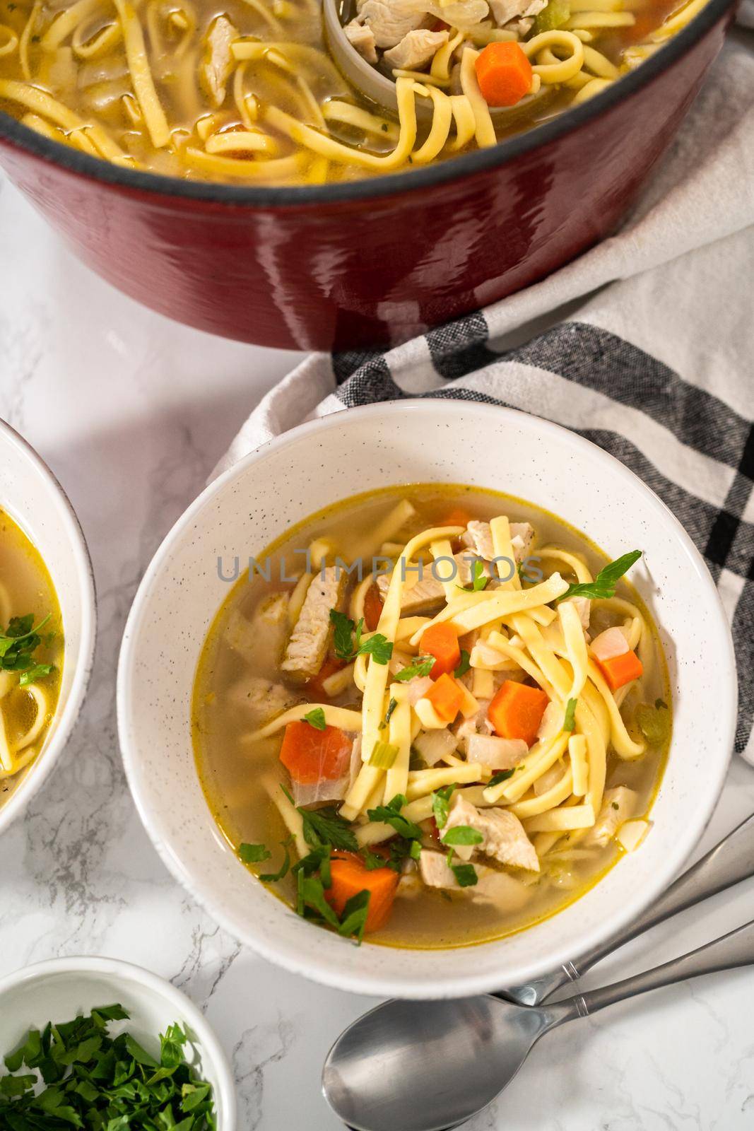 Serving chicken noodle soup with kluski noodles in white ceramic soup bowls.