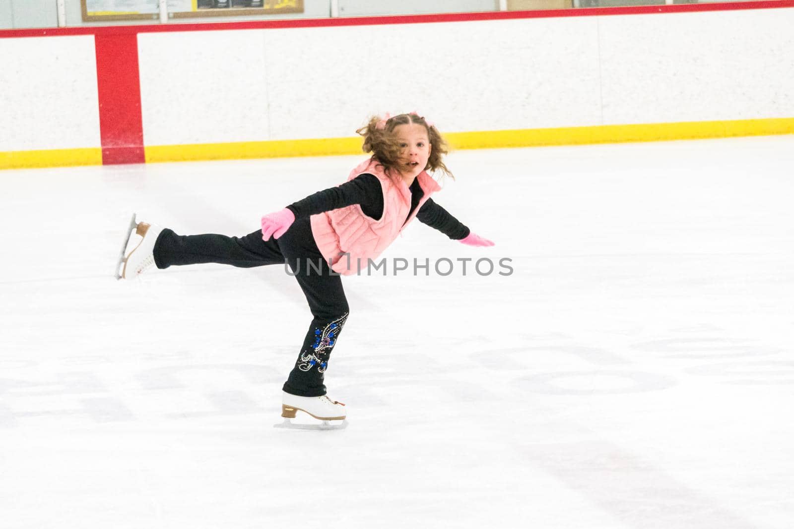 Little girl practicing figure skating moves on the indoor ice rink.