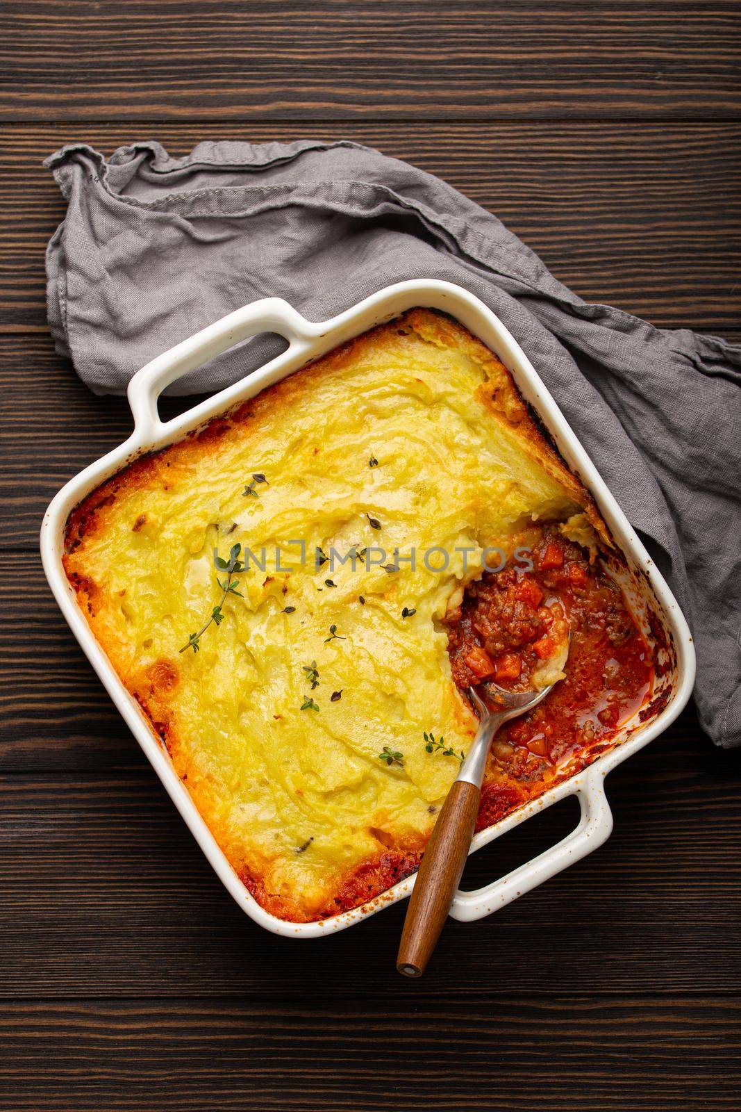 Traditional dish of British cuisine Shepherd's pie casserole with minced meat and mashed potatoes in ceramic baking dish on white rustic table with spoon from above