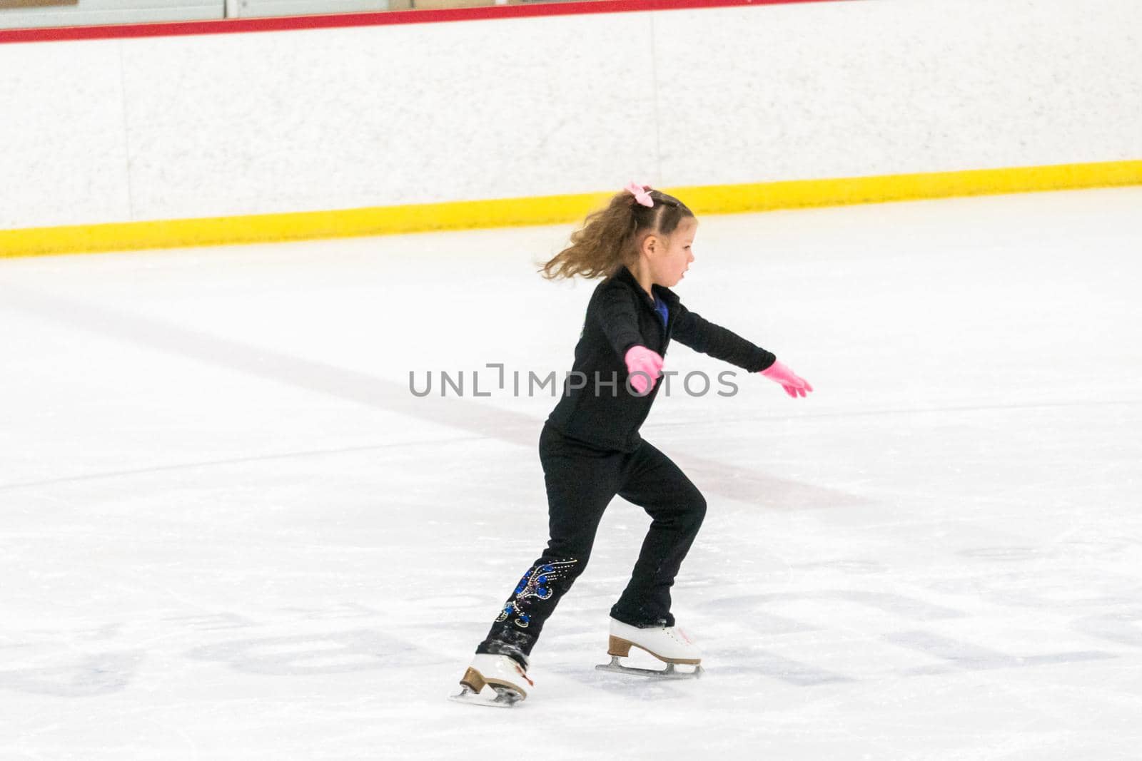 Little girl practicing figure skating moves on the indoor ice rink.