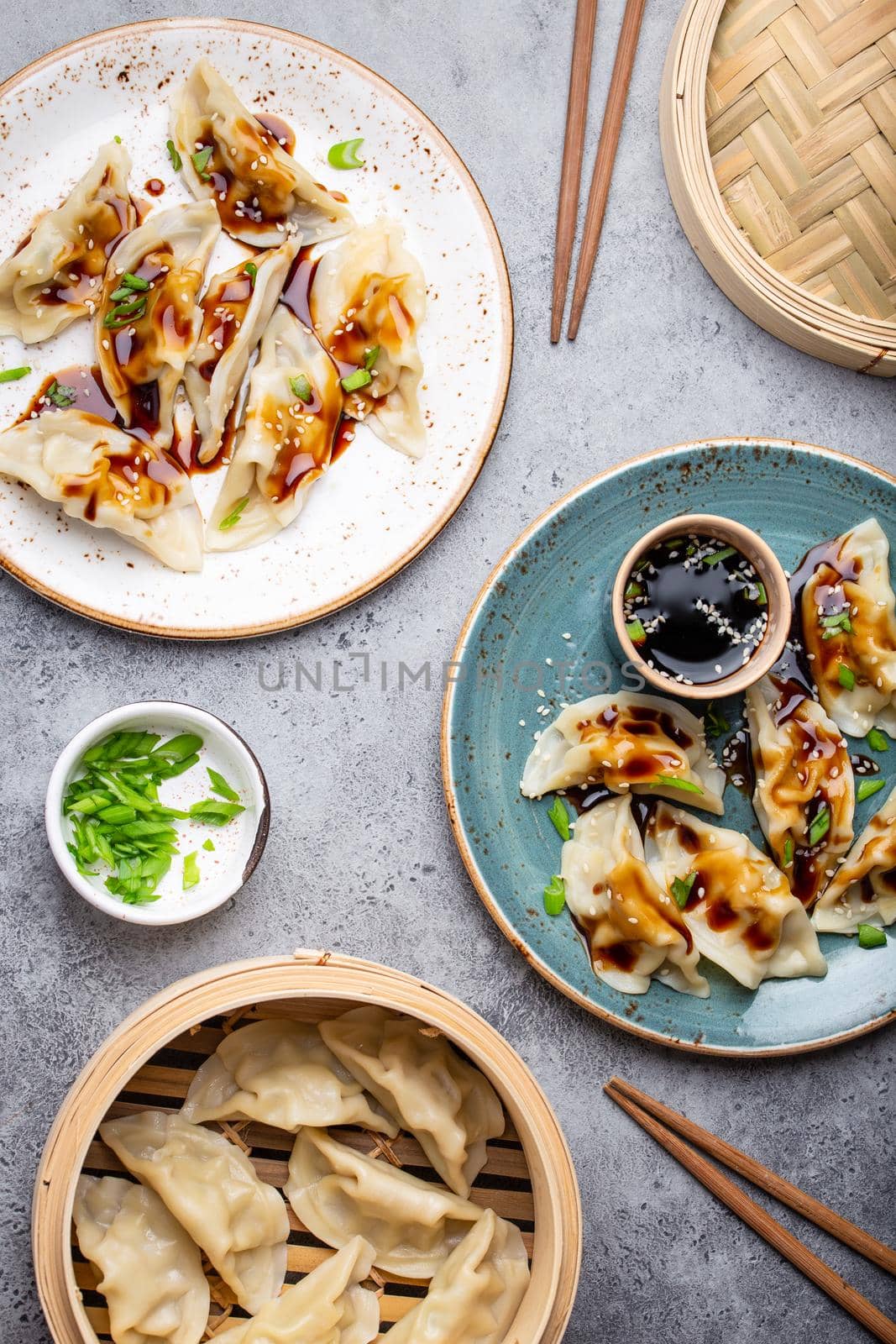 Close-up, top view of two plates with traditional Asian dumplings with soy sauce and chopsticks on gray rustic stone background. Authentic Chinese cuisine