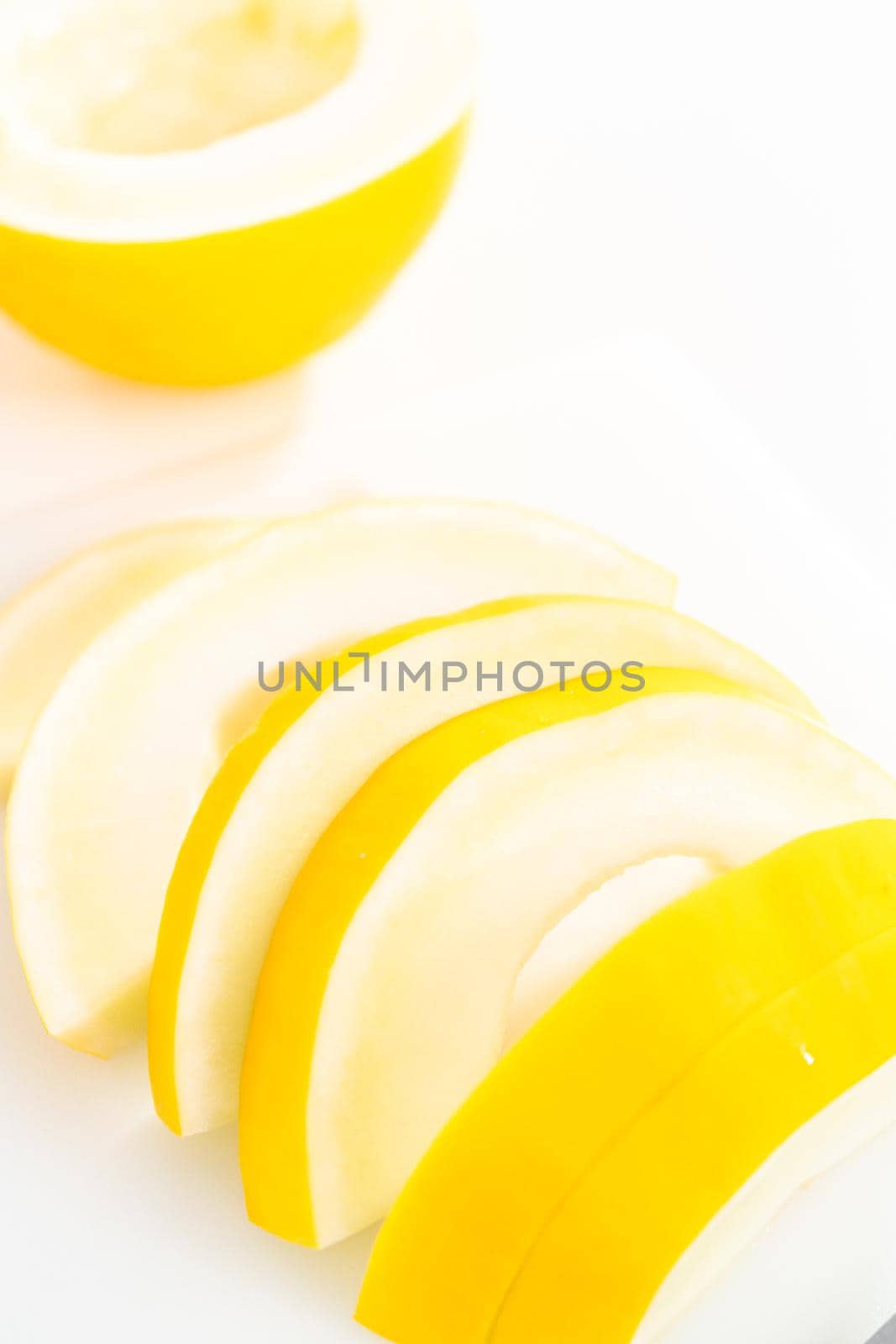 Slicong golden dewlicious melon on a white cutting board.