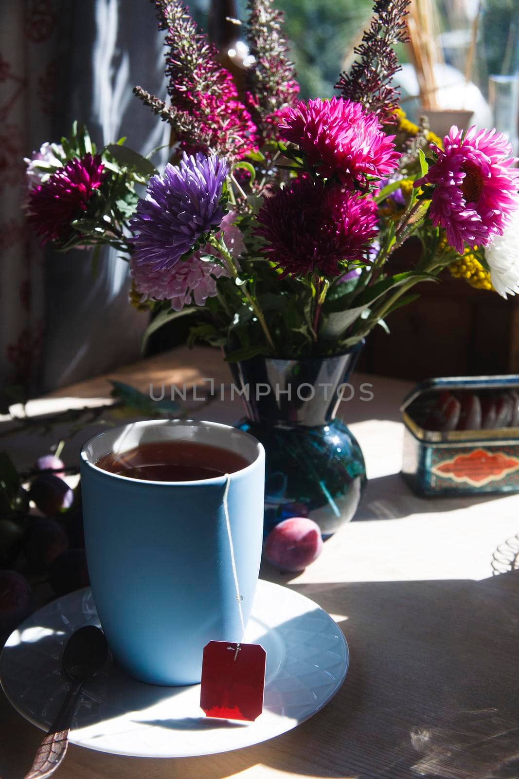 Blue cup of tea with bouquet of blue, pink and purple aster flowers in th bright light, morning tea concept, selective focus.