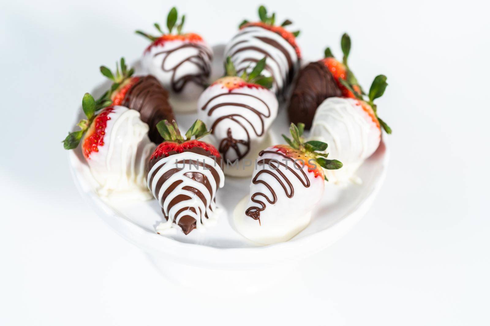 White and dark chocolate dipped strawberries on a white cake stand.