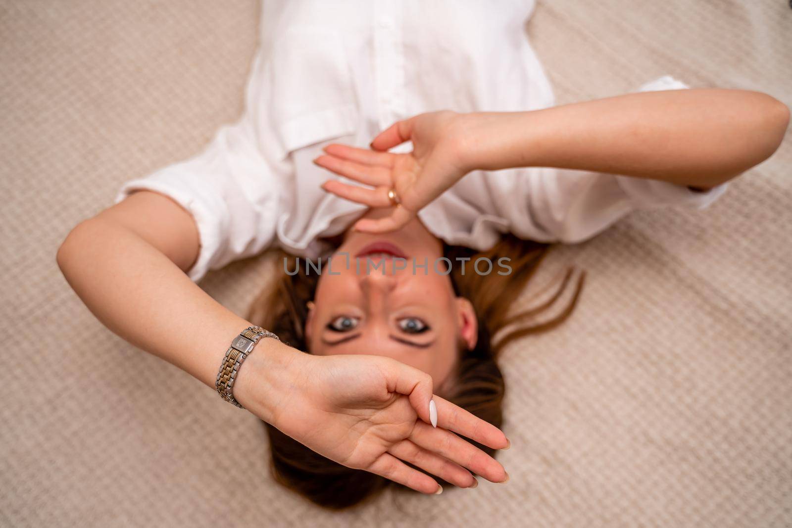 The woman lies on the bed on her back, top view. She looks straight ahead, wearing a white shirt.