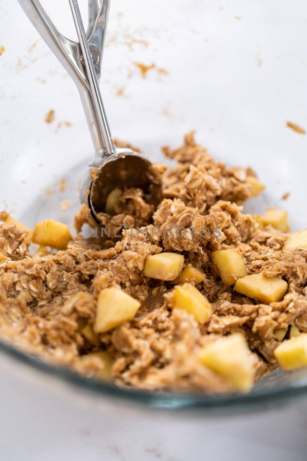 Scooping cookie dough into the baking sheet lined with parchment paper to bake apple oatmeal cookies.