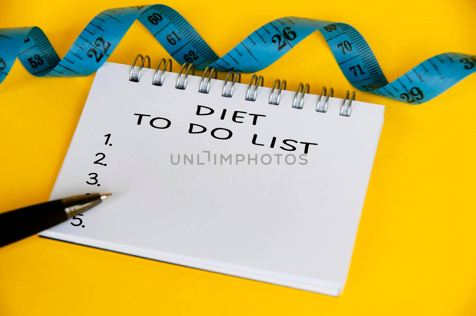 Diet to do list text on white notepad with blue measuring tape on yellow background. Health and diet concept.