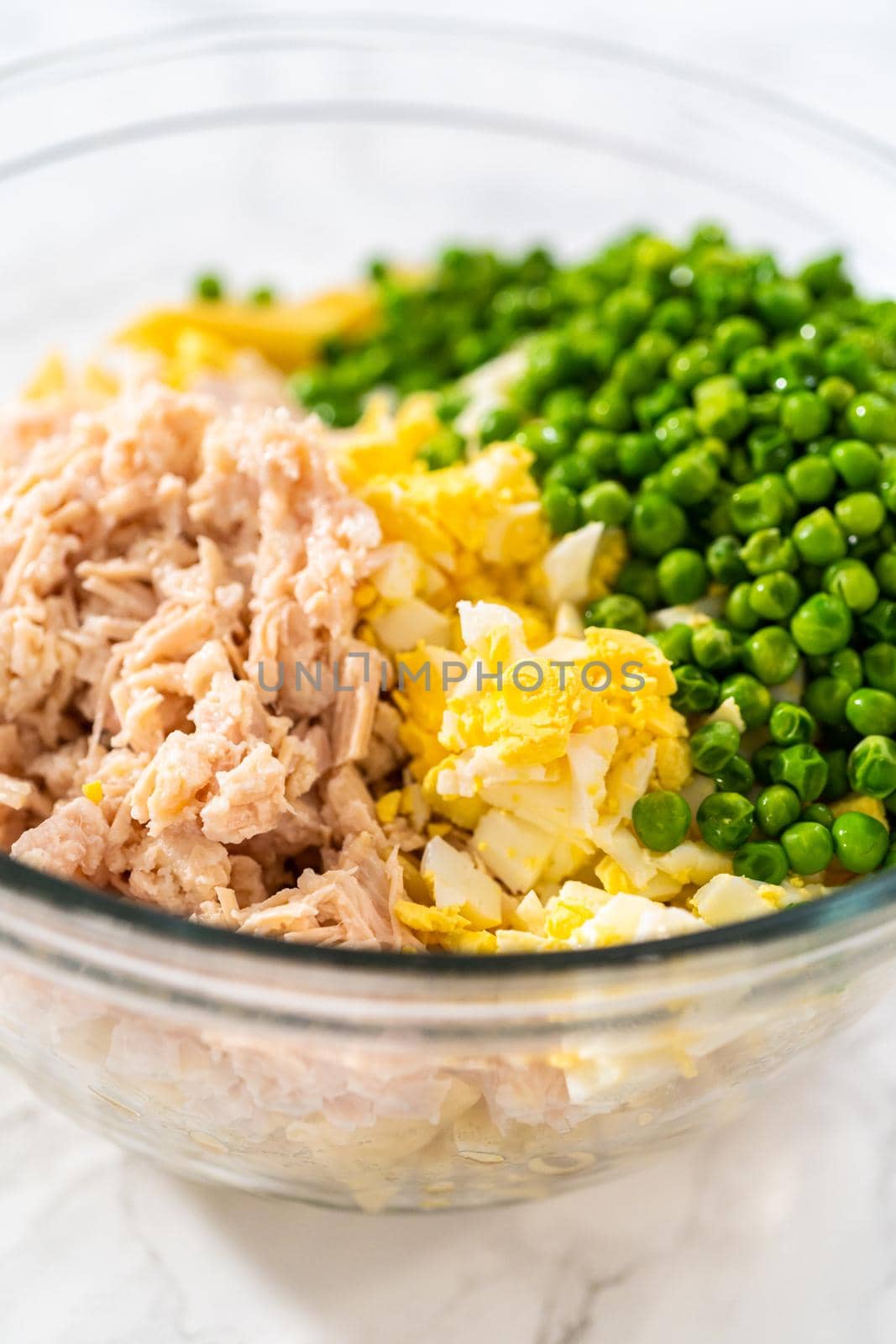 Mixing ingredients in a large glass mixing bowl to make macaroni salad with chicken.