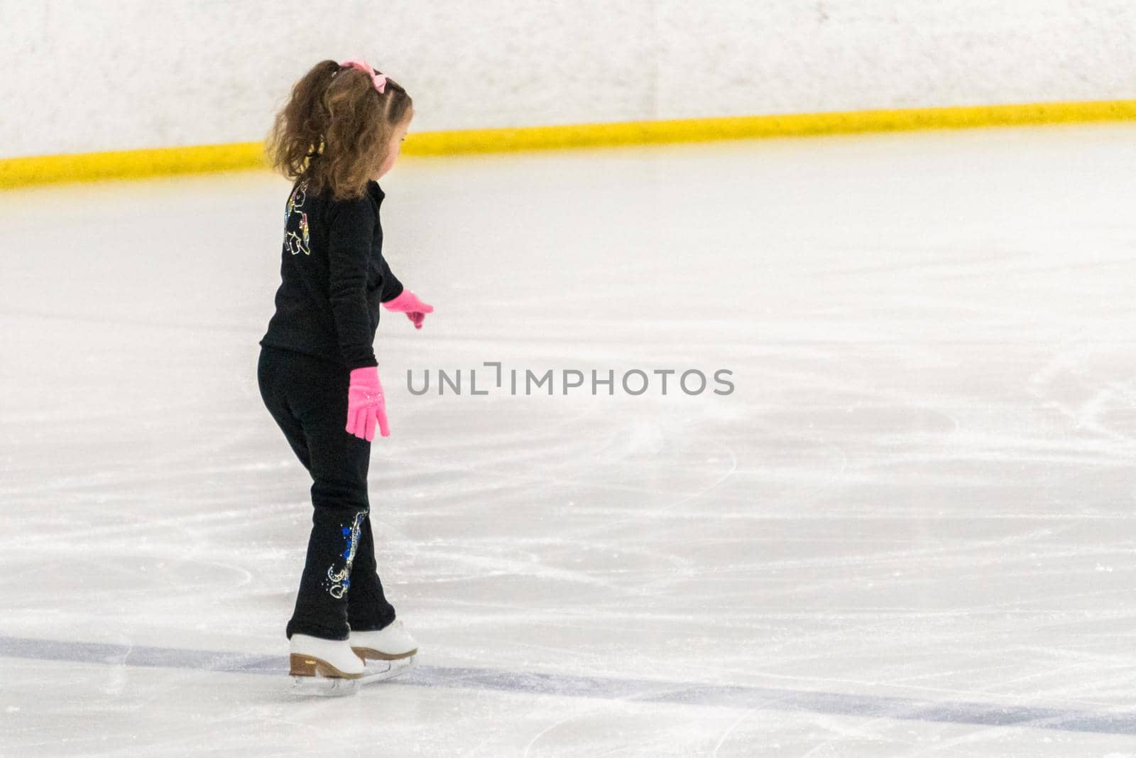 Little girl practicing figure skating moves on the indoor ice rink.