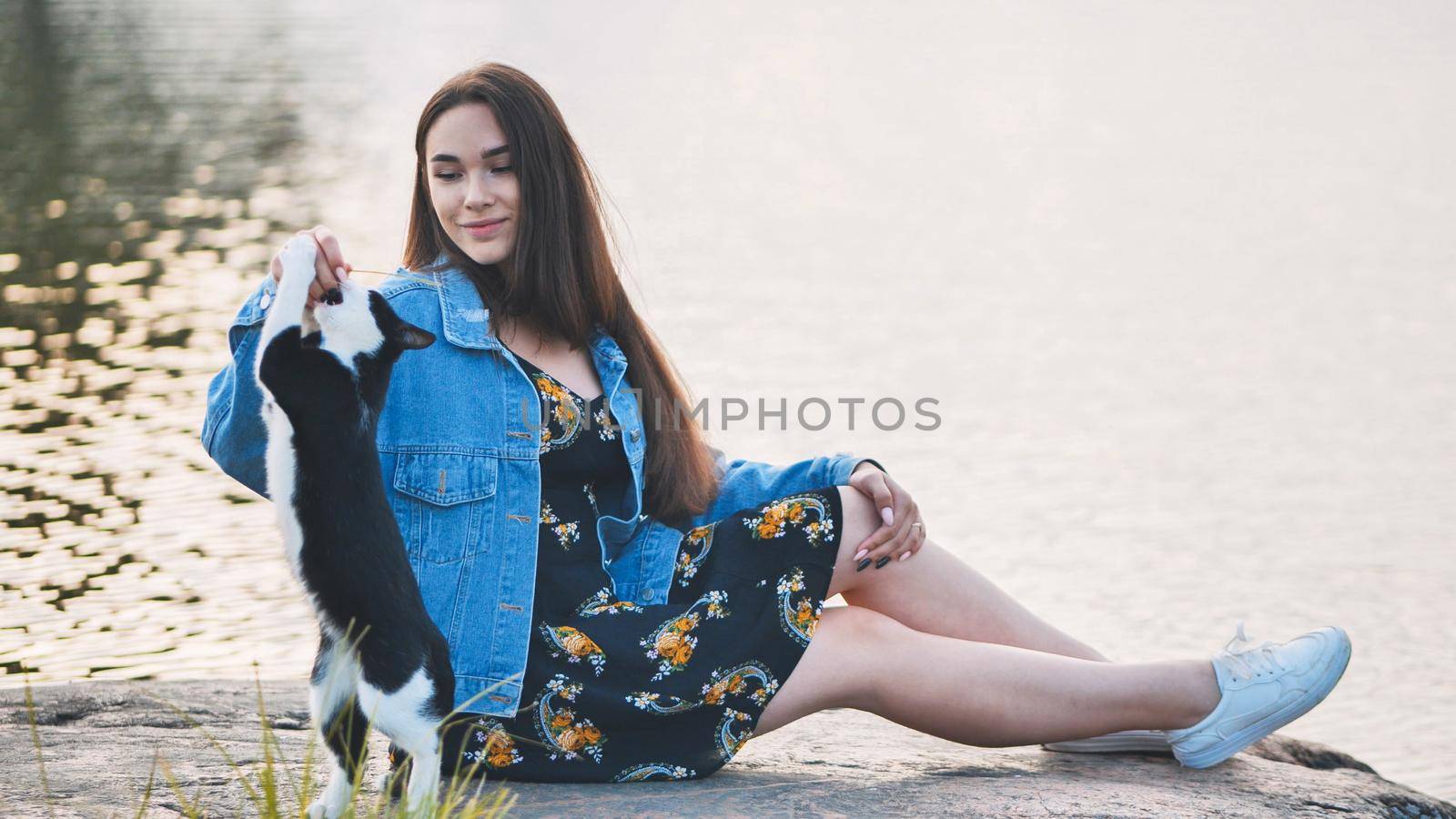 A girl plays with a cat by the lake