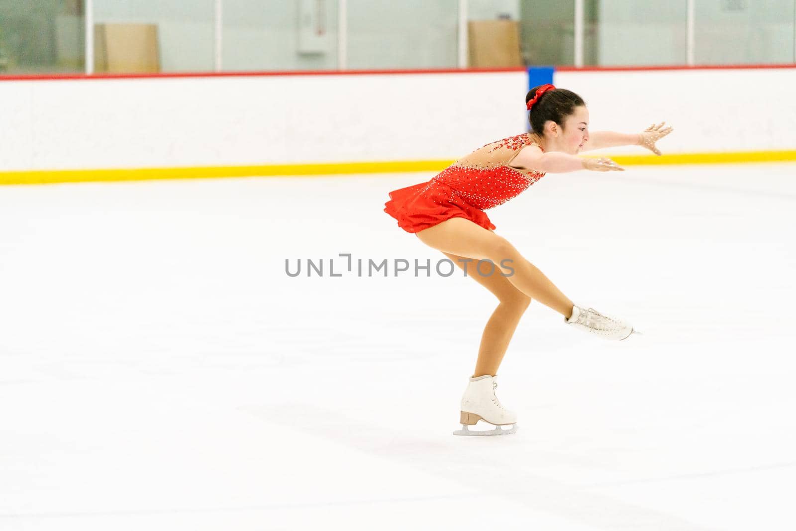 Teenage girl practicing figure skating on an indoor ice skating rink.