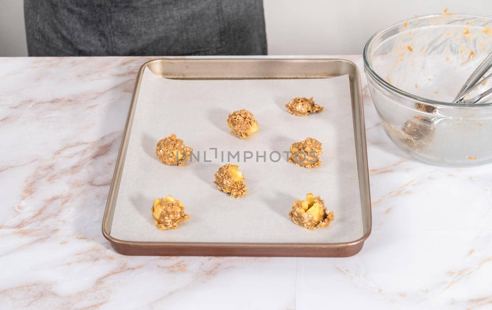 Scooping cookie dough into the baking sheet lined with parchment paper to bake apple oatmeal cookies.