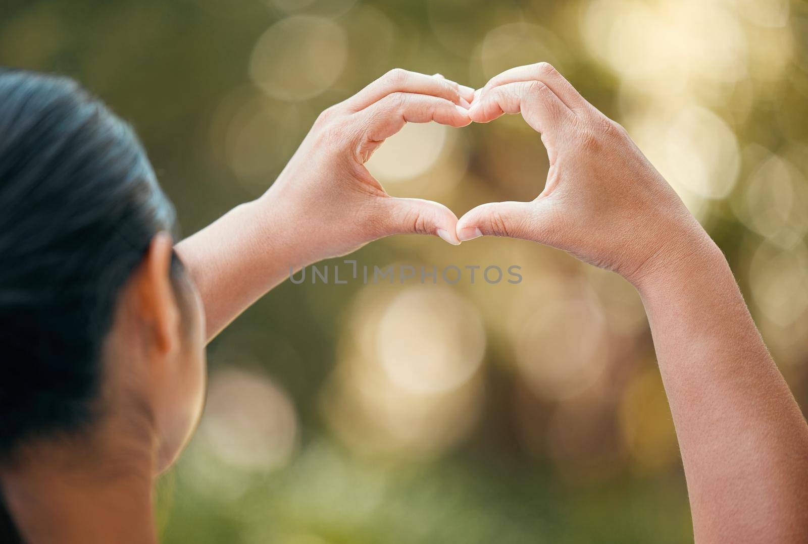 Woman use hands, make heart or love sign outside with bokeh in nature background. Lady with fingers together, show icon or expression of romance against outdoor backdrop with blurred natural light.
