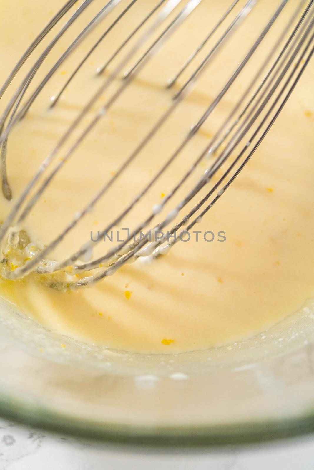 Mixing wet ingredients in a large glass mixing bowl to bake lemon cupcakes.